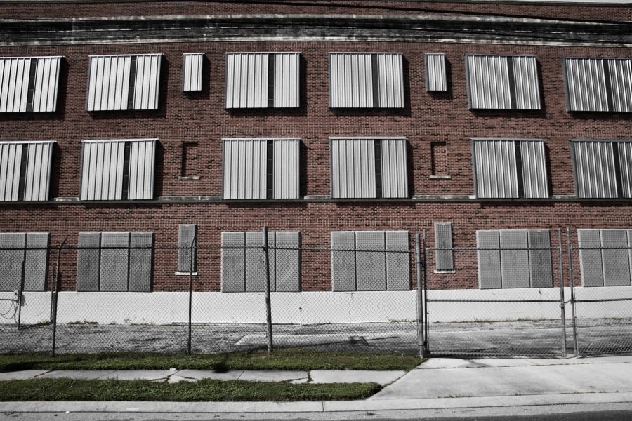 A partially black and white, partially color photo of a brick wall, behind a chainlink fence with some grass in the foreground in the 7th Ward of New Orleans, Louisiana.