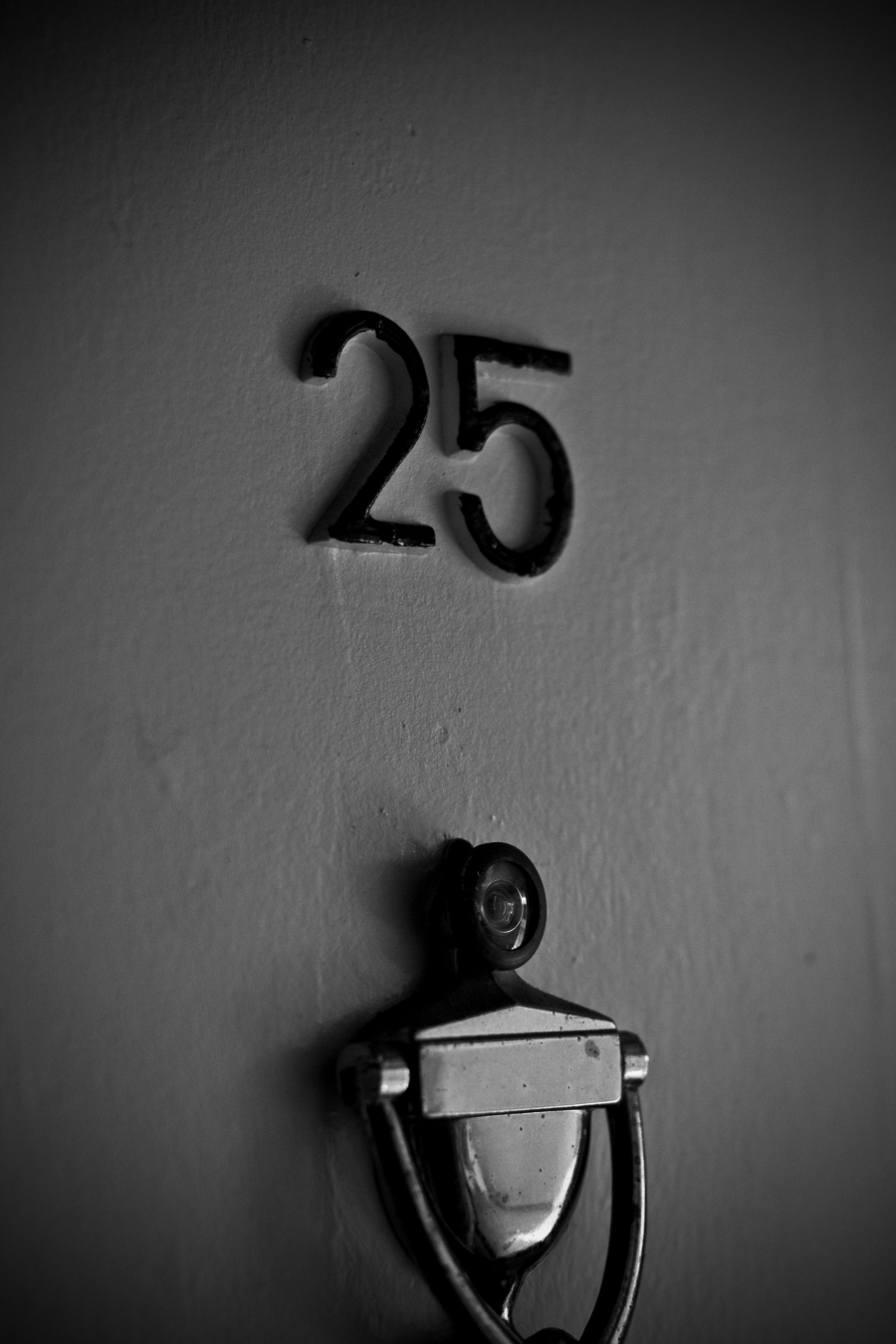 Address numbers reading 25 hung on a door with a door knocker and a peephole in black and white.